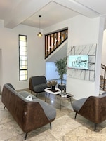 Uma sala de estar moderna com um conjunto de sofás, uma mesa de centro, um vaso de planta e uma televisão na parede.