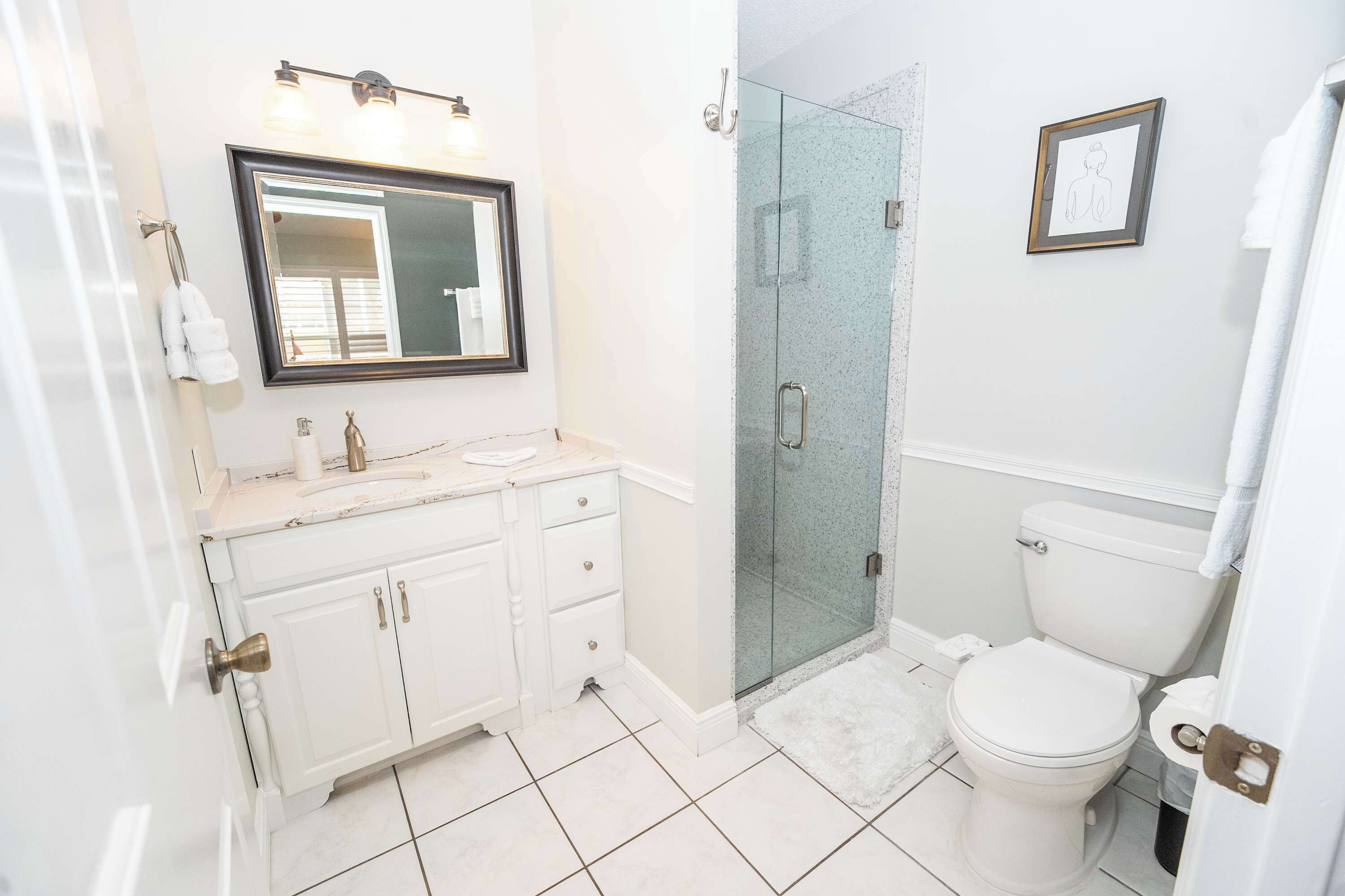 A bathroom with a white vanity, a glass shower enclosure, and a toilet.