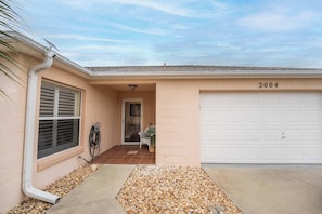 A residential building with a garage, a door with a number '2004' above it, a window with shutters, and a small porch area with a chair and a plant. - Private Spa, 2 seater golf cart, Life Style ID's (Lady Lake)