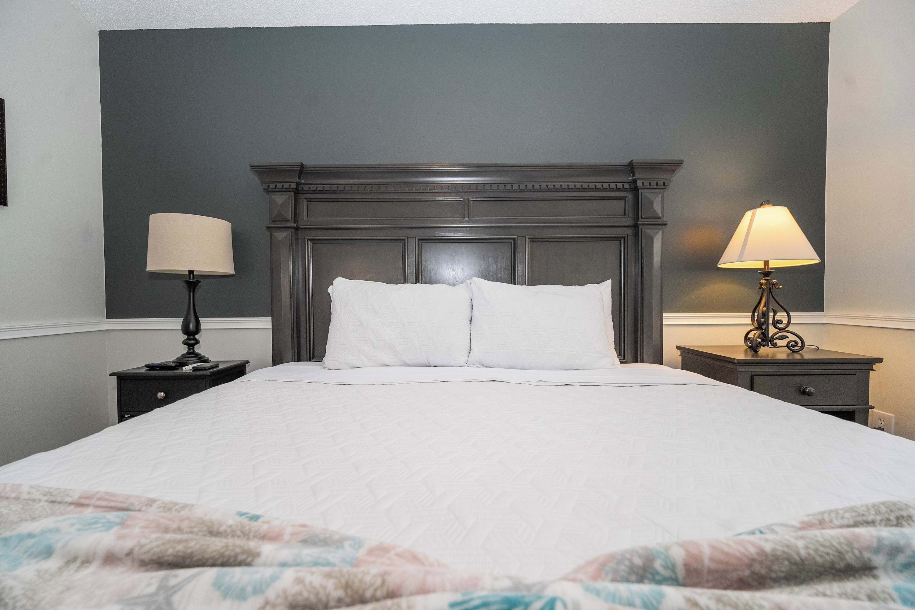 A neatly made bed with white linens, a dark wooden headboard, and two bedside tables with lamps.