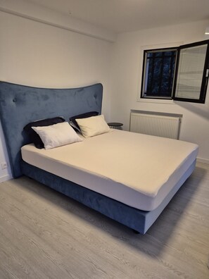 Ein modernes Schlafzimmer mit einem großen Bett, einer Kopfteil und einem Fenster mit Jalousien.
