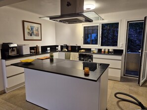 A modern kitchen with a central island, a coffee machine, and a window with a view of trees. - Wonderful villa with a view of the sea (Saint-Raphaël)