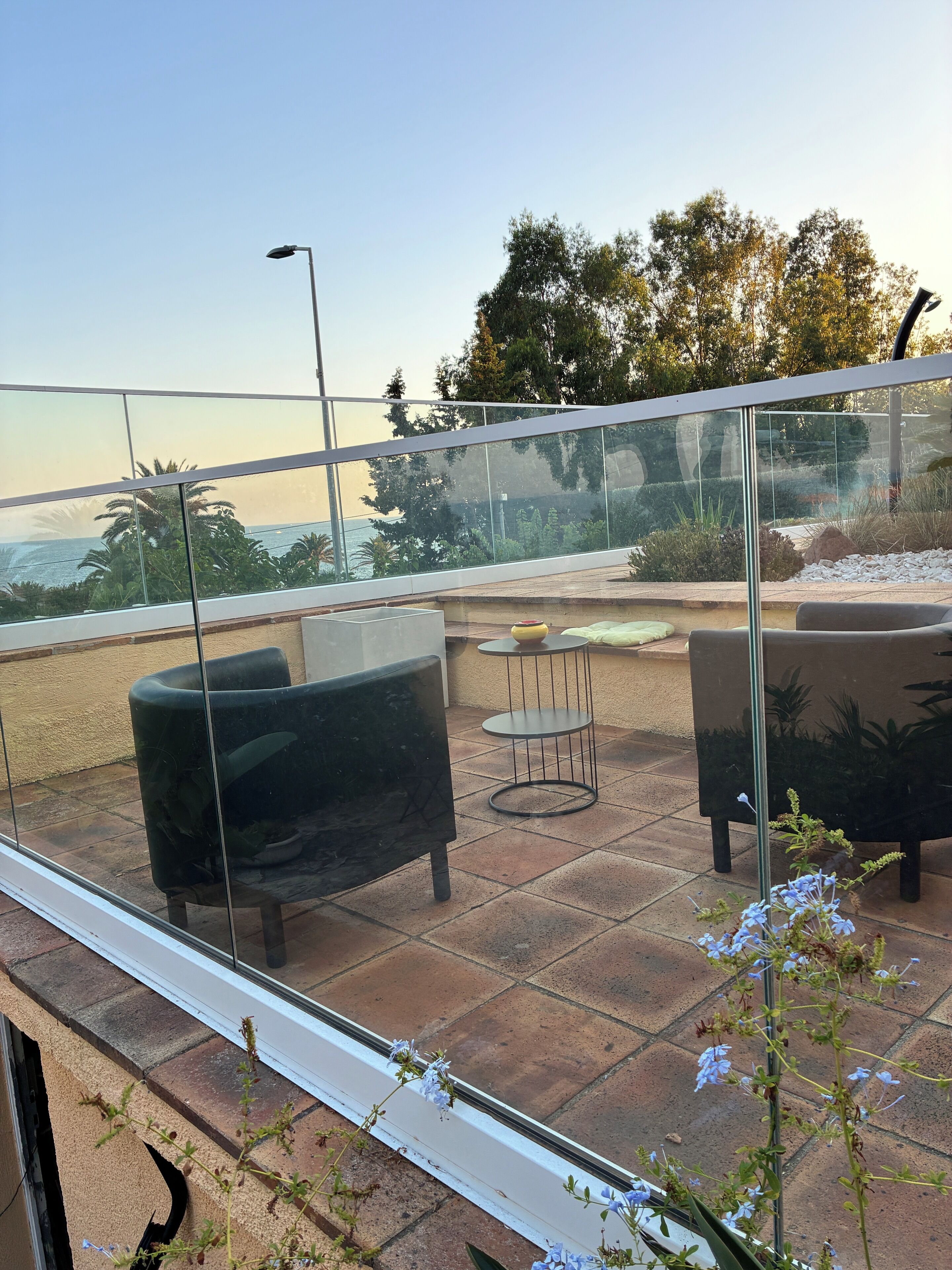 A balcony with outdoor seating, a view of the sea, and a glass railing.