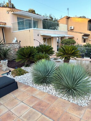 A residential property with a patio area featuring a stone wall, a black outdoor seating area, and a variety of green plants. - Wonderful villa with a view of the sea (Saint-Raphaël)