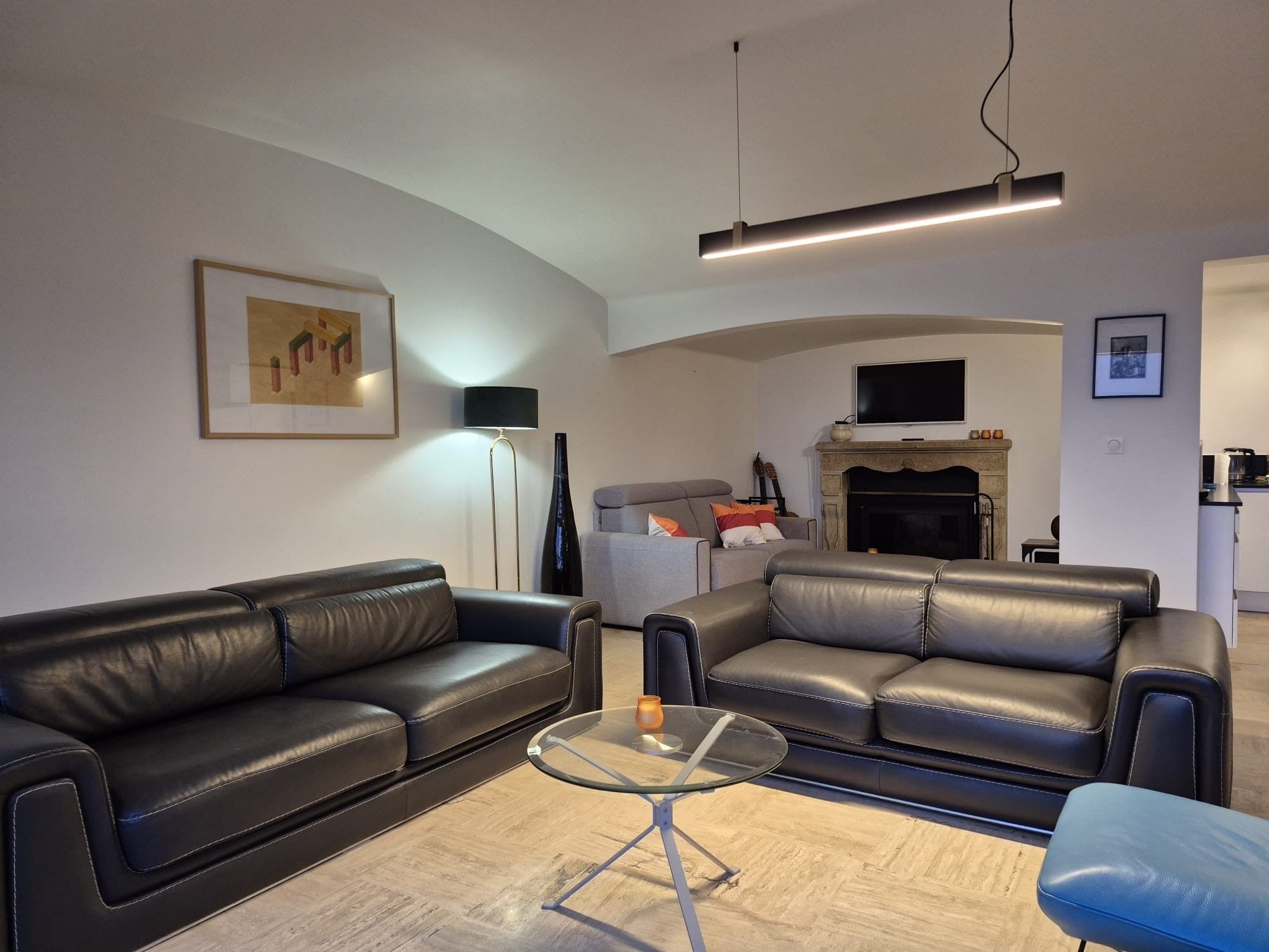 A living room with two black leather sofas, a glass coffee table, a fireplace, and a flat-screen TV mounted above it.