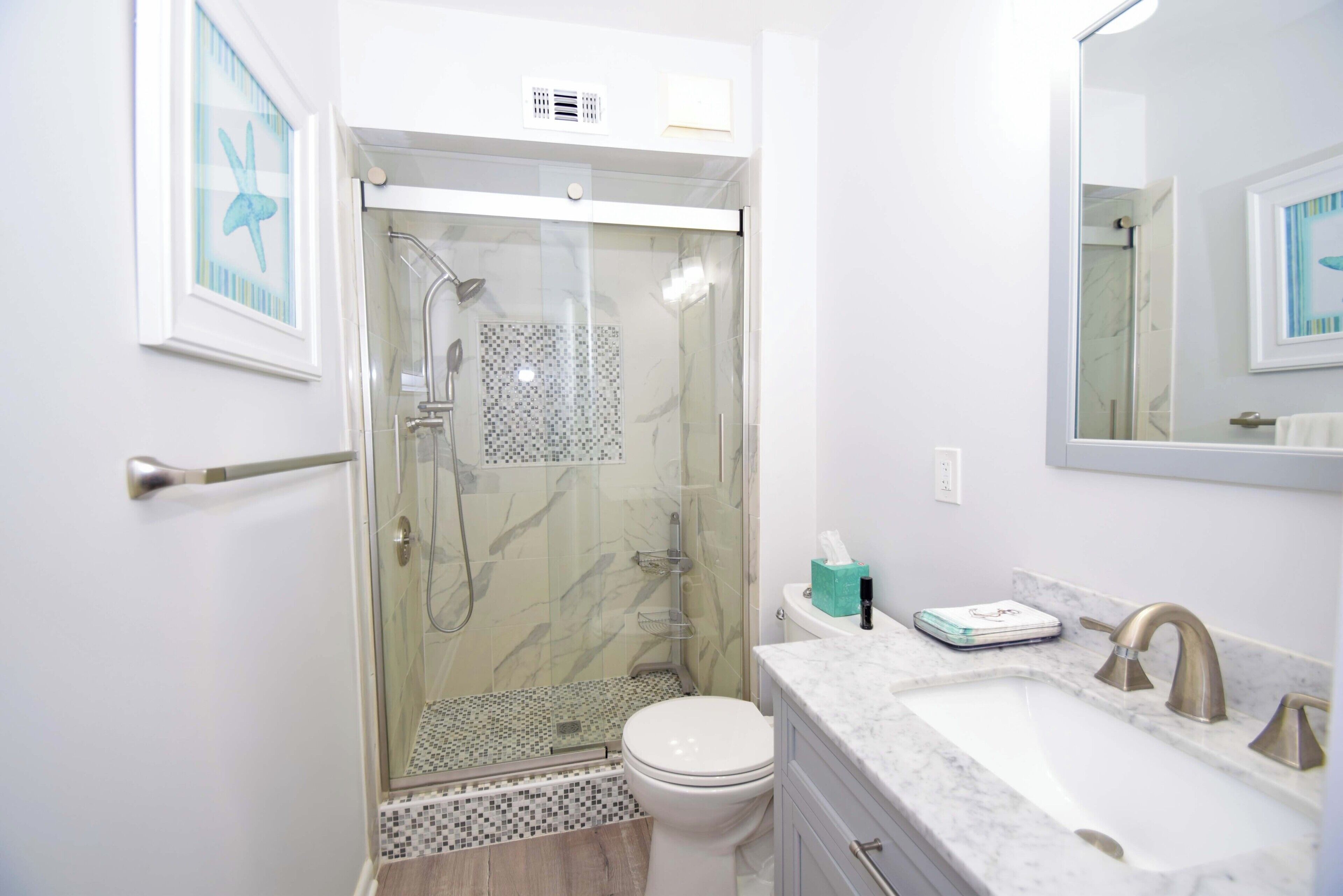 A bathroom with a glass-enclosed shower, a toilet, a sink with a marble countertop, and a mirror.