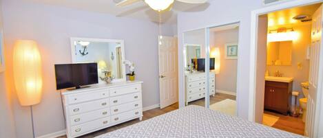 A bedroom with a bed, a TV, a dresser, a mirror, and a ceiling fan.