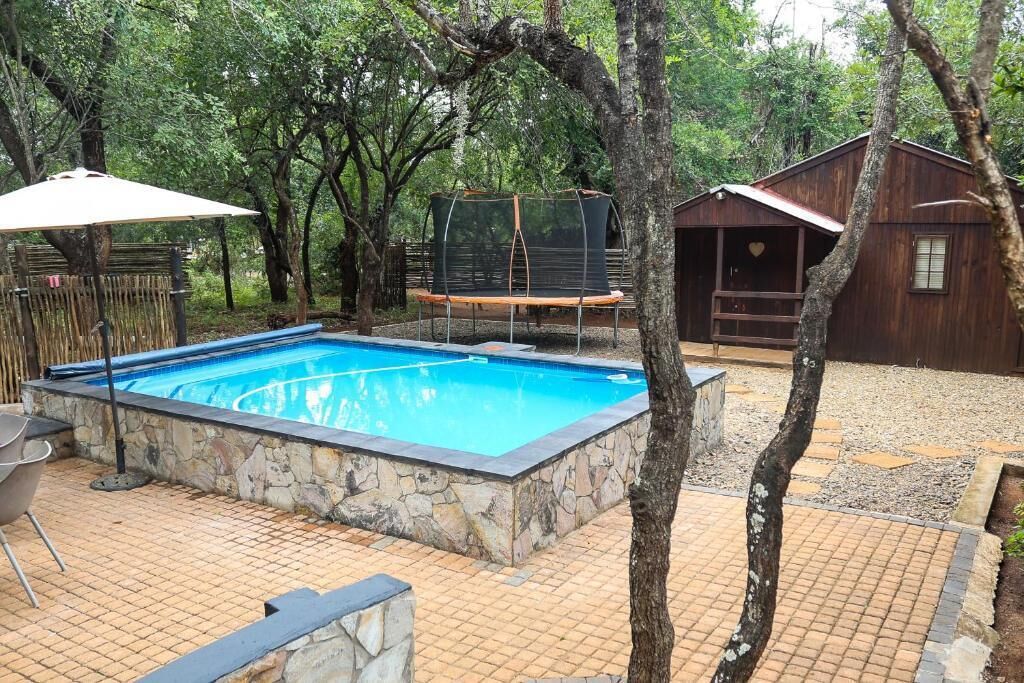 A swimming pool with stone borders, a wooden deck, and a small wooden building.
