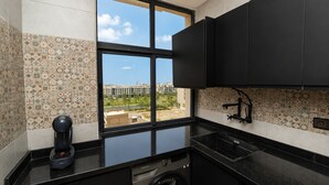 Una cocina moderna con cafetera, lavadora y vista a la ciudad a través de un ventanal amplio.