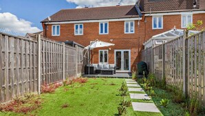 Un immobile residenziale con una casa in mattoni, un cortile recintato e una zona patio con mobili da esterno.