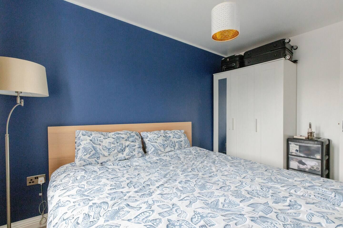 A bedroom with a bed, a nightstand, a lamp, a wardrobe, and a suitcase on the floor.