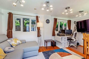 Ein modernes Wohnzimmer mit einer Couch, einem Schreibtisch mit Computer, einer Lampe und einem großen Fenster.