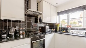 Una cucina moderna con mobili bianchi, zoccolo a mosaico nero e elettrodomestici in acciaio inossidabile.
