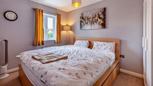 Una camera da letto con un letto, una sveglia a parete, una finestra con tende, una lampada e un quadro.