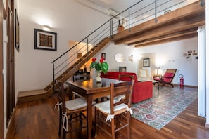A dining area with a wooden table, chairs, a red sofa, and a staircase. - Elegant 57 dqm apartment, for up to 4 guests, located on the second floor of a renovated period building with lift (steps to access). The property is located in the center of Palermo, in an authentic and folkloristic neighborhood in the Vucciria area, th (Palermo)