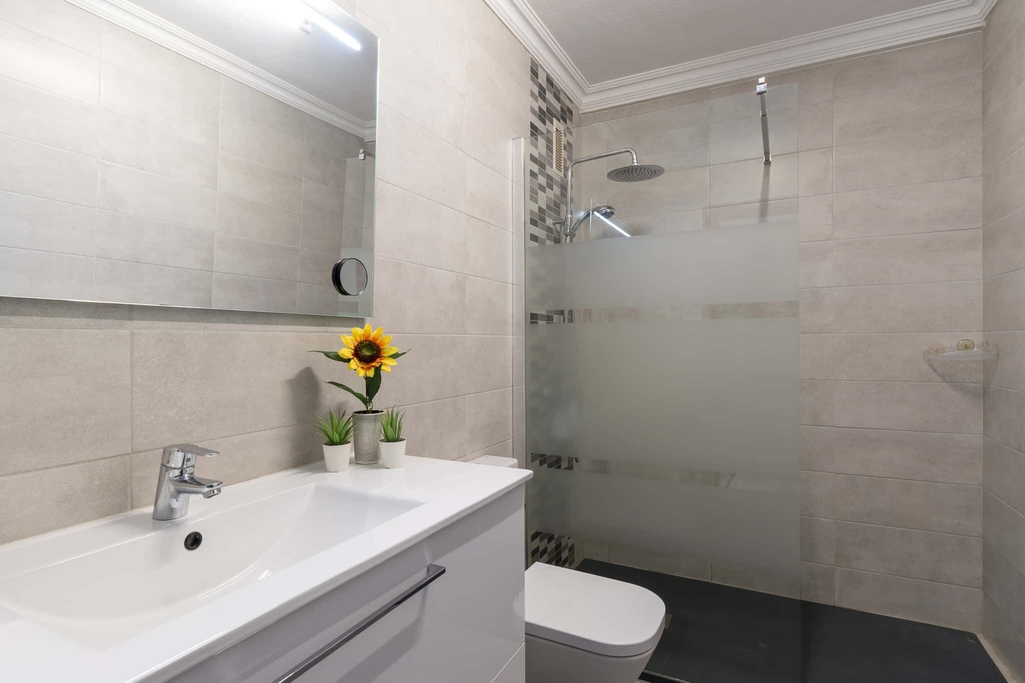Een badkamer met een wit wastafelmeubel, een spiegel, een toilet en een douche met glazen wanden.