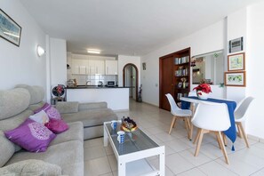 A living room with a sofa, coffee table, and dining area with chairs and a table. - Paloma Beach 15 - One Bed Penthouse (Los Cristianos)