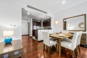 A modern dining area with a wooden table, white upholstered chairs, and a blue lamp. - Free Housekeeping Visits During Your Stay - Stayshort - Elegant 1BR Apartment With Amazing Palm Views (Dubai)
