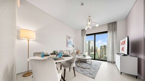 Habitación de hotel moderna con zona de comedor, televisor y balcón con vistas a la ciudad.