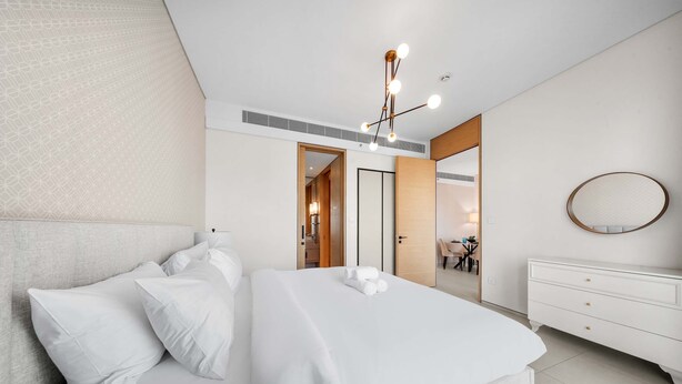 Una habitación de hotel moderna con una cama grande, un tocador blanco, un espejo redondo y una lámpara en el techo.