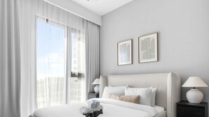 Una habitación de hotel moderna con una cama grande, una mesita de noche con lámpara y vistas a la ciudad.