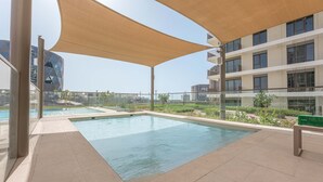Una piscina en la azotea con una pérgola, rodeada de edificios modernos y un cielo despejado.