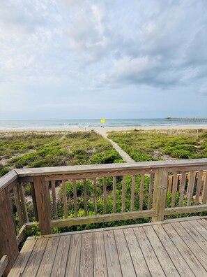A wooden deck with a view of a beach and a pier.