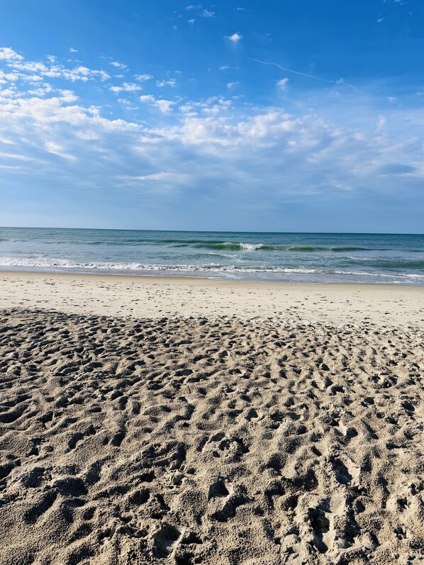 A sandy beach with footprints leading to the water, a clear sky, and a calm sea.