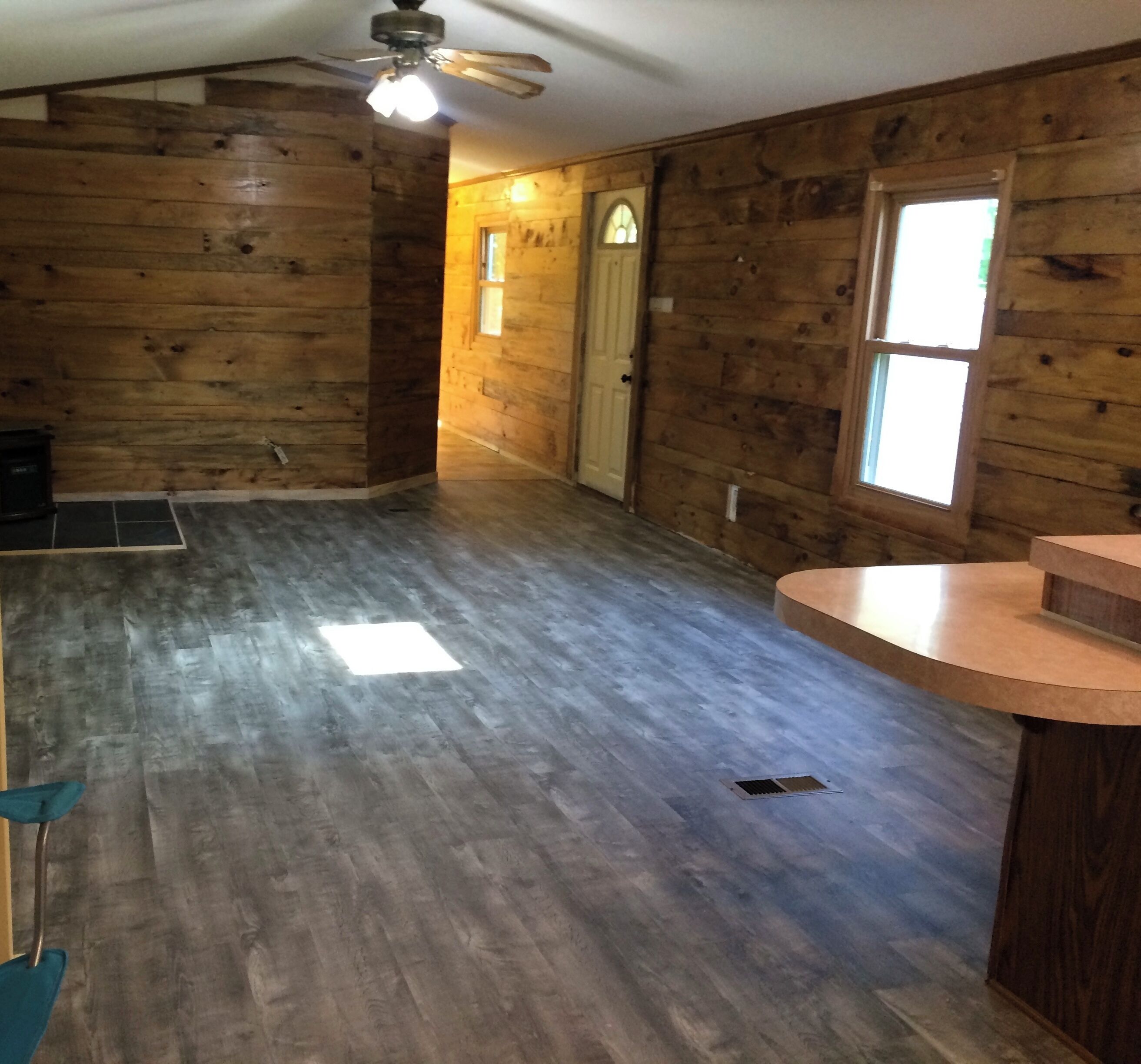 A room with wooden walls, a ceiling fan, a window, and a door.