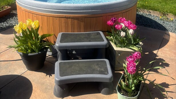 Un jacuzzi con escalones de madera y tulipanes en macetas en un jardín.