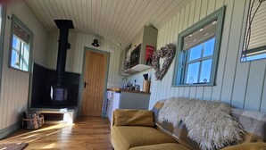 Una sala de estar acogedora con sofá, chimenea, piso de madera y una zona de cocina con ventana.