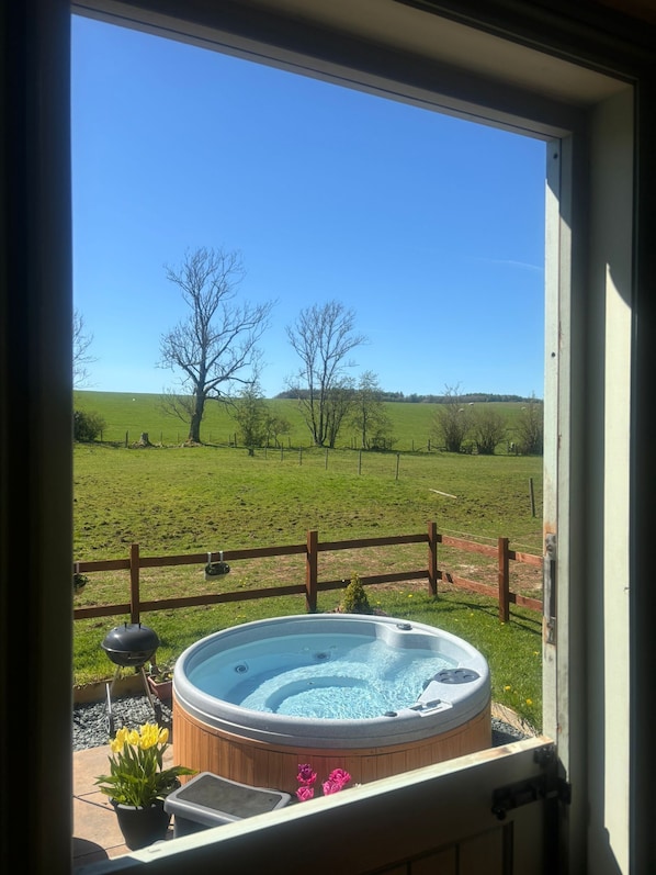 A hot tub with a wooden exterior, a view of a green field, and a wooden fence.
