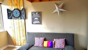 A grey sofa with colorful pillows, a dartboard, a wall-mounted star decoration, and a sign reading 'Burger House.' - Normandy cocoon valley view terrace-7 min Honfleur (Fourneville)