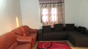 A living room with a brown leather sofa, a dark sofa, and a red rug with abstract patterns. - Saint Louis Sénégal Yaga Immo Gandon Émetteur (Gandon Émetteur)
