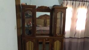 A wooden cabinet with glass doors, a bed with a patterned bedspread, and a window with curtains. - Saint Louis Sénégal Yaga Immo Gandon Émetteur (Gandon Émetteur)