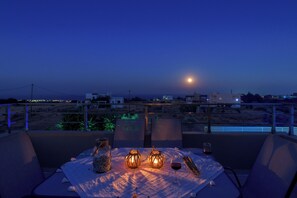 A table set for two with candles, a glass of red wine, and a candle holder on a balcony overlooking a desert landscape at night. - Melodia Home: Private Pool-Scenic Sea View-Hilltop (Rhodes)