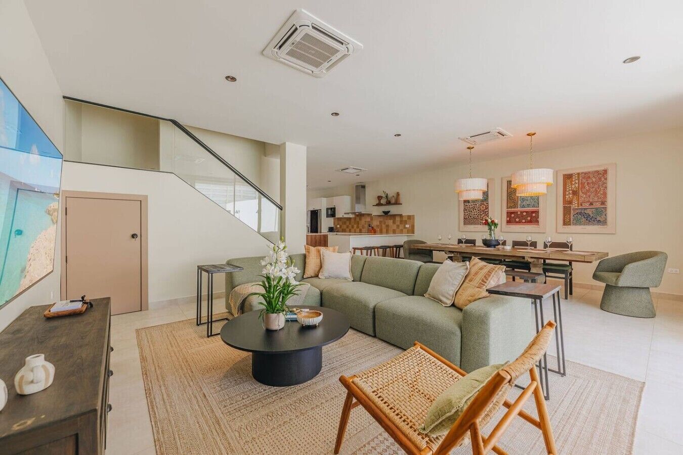 A modern living room with a green sofa, a coffee table, and a wicker chair. There is a staircase leading to an upper level.