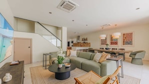 Una sala de estar moderna con un sofá verde, una mesa de centro y una silla de mimbre. Se ve una escalera que sube a un nivel superior.