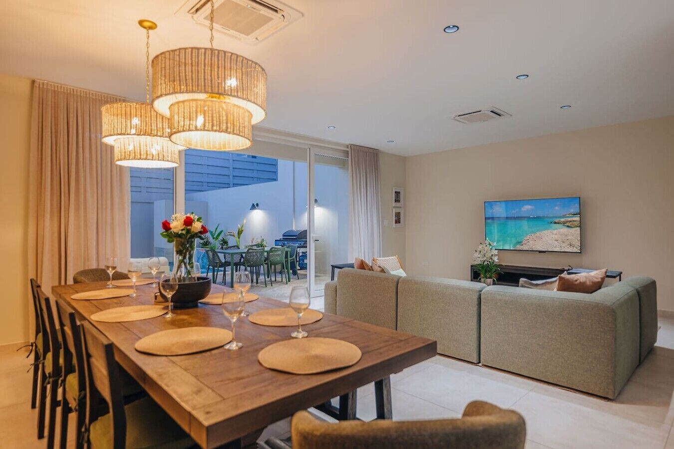 A modern living room with a dining area, a sofa set, and a TV displaying a beach scene.