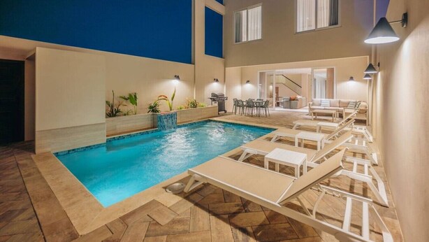 Piscina con sillas de descanso, zona de barbacoa y una escalera que lleva a un nivel superior.