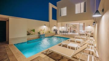 A swimming pool with lounge chairs, a barbecue area, and a staircase leading to an upper level.