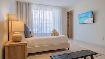 A hotel room with a bed, a bedside lamp, a small table, a painting on the wall, and a view through the window.