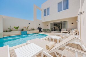 A pool area with lounge chairs, a barbecue, and a building with a modern design. - 1min walk Boca Catalina Beach, 4, bedrooms, Private Pool, Tub, 10 sleeps (Noord)