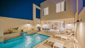 Un área de piscina con sillones reclinables, una parrilla y una zona de comedor.