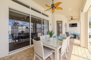 A glass-top dining table with chairs, a ceiling fan, and a view of the outdoor patio. - Game room - sleeps 8 with large pool! (Cape Coral)