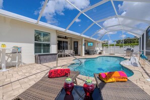 A pool area with a covered patio, lounge chairs, and a poolside table. - Game room - sleeps 8 with large pool! (Cape Coral)