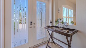 Un vestíbulo con dos puertas de cristal, una consola decorada y una ventana con persianas.