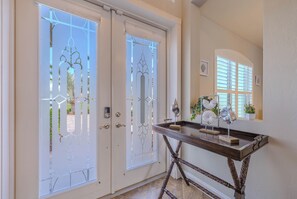 A foyer with two glass doors, a console table with decorative items, and a window with blinds. - Game room - sleeps 8 with large pool! (Cape Coral)