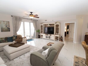 A living room with a sofa, a television, and a ceiling fan. - Balconies with stunning views from Master Bedroom and Living Room (Miramar Beach)