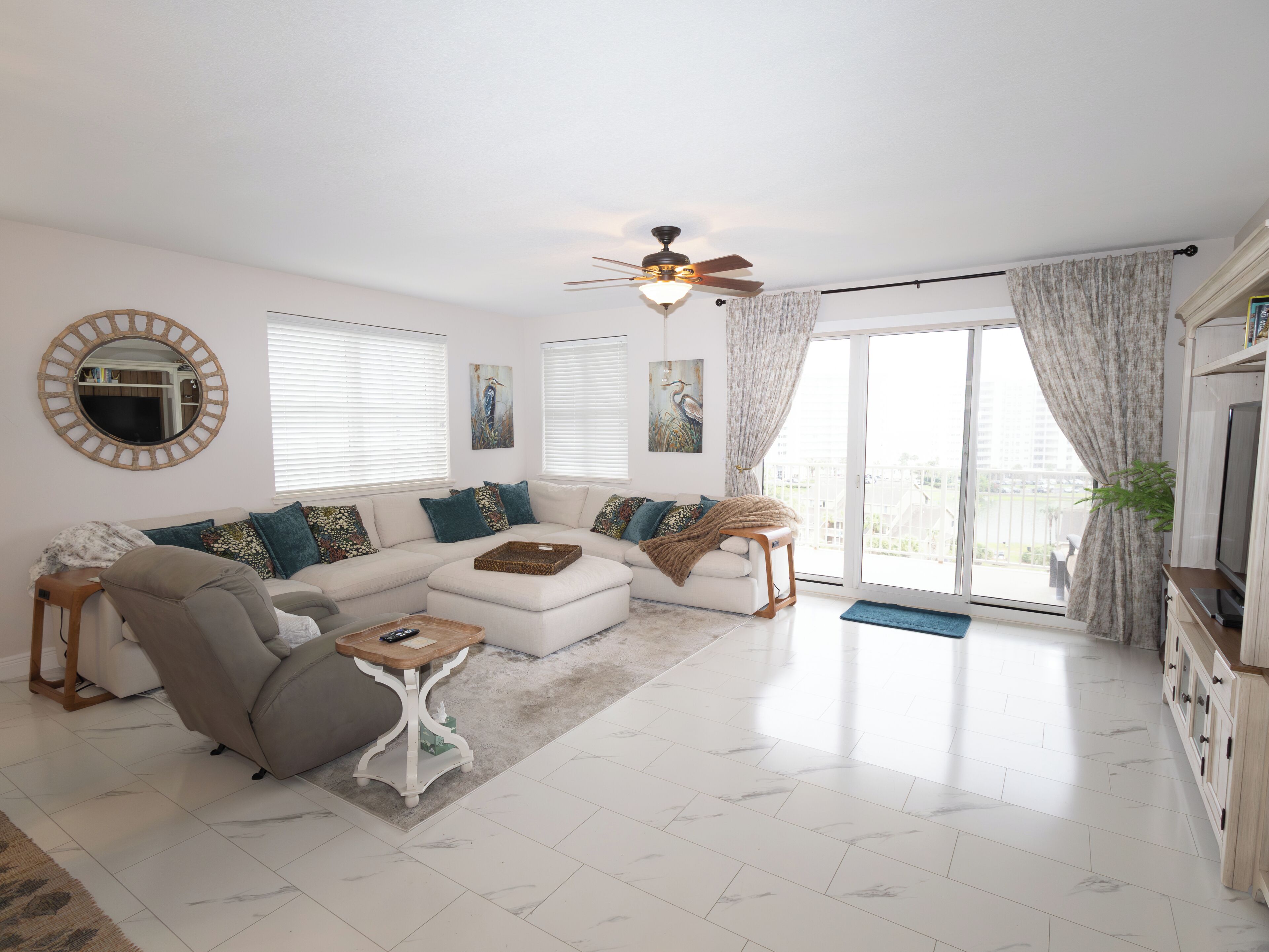 A living room with a sectional sofa, a small table, a ceiling fan, and a large sliding glass door leading to an outdoor area.